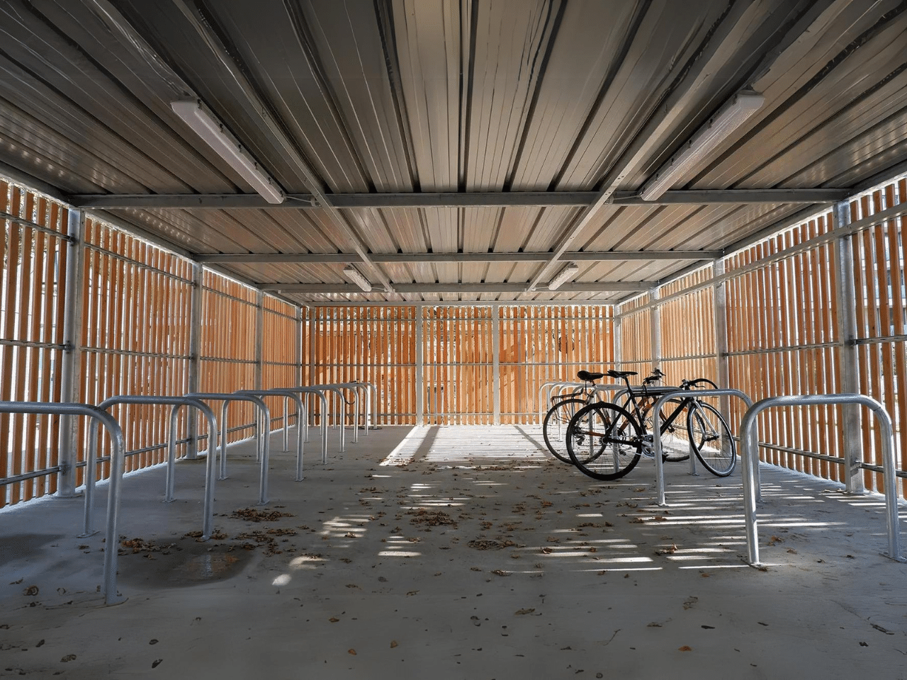 Intérieur d'un abri refuge ByCommute en bois avec structure en acier galvanisé, équipé de racks à vélos sécurisés. Idéal pour le stationnement de vélos dans les entreprises et collectivités, offrant un espace abrité et sécurisé.
