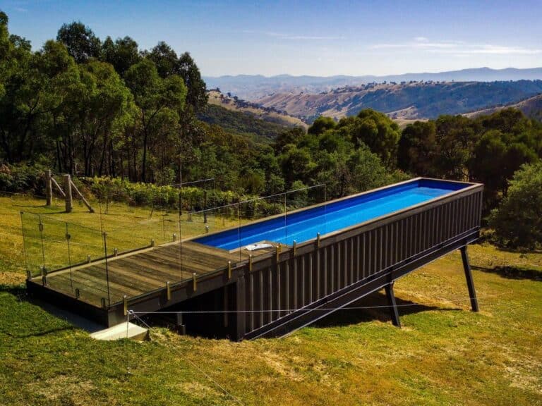 Piscine en container surélevée avec terrasse en bois, située dans un paysage vallonné.