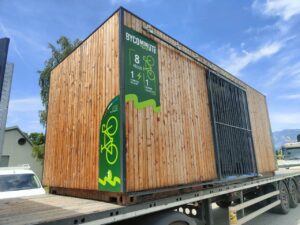 Abri vélo bois Bycommute sur un camion de transport, conçu pour accueillir jusqu'à 16 vélos avec des panneaux solaires intégrés et un service électronique sécurisé.